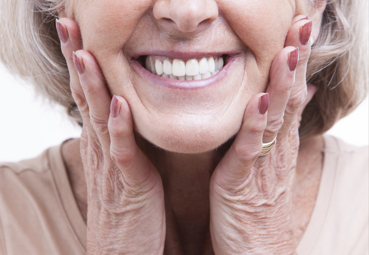 The image is a close up of senior woman with dentures smiling and holding her face. It represents the different types of dentures.